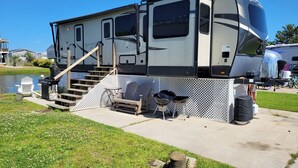 A recreational vehicle with a covered porch, outdoor seating, and a staircase leading to the upper level. - Luxurious RV (Virginia Beach)