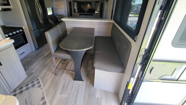 A compact RV kitchen with a stove, refrigerator, and seating area. - Luxurious RV (Virginia Beach)