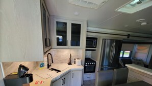 A compact kitchen with white cabinets, a microwave, a stove, and a refrigerator. - Luxurious RV (Virginia Beach)