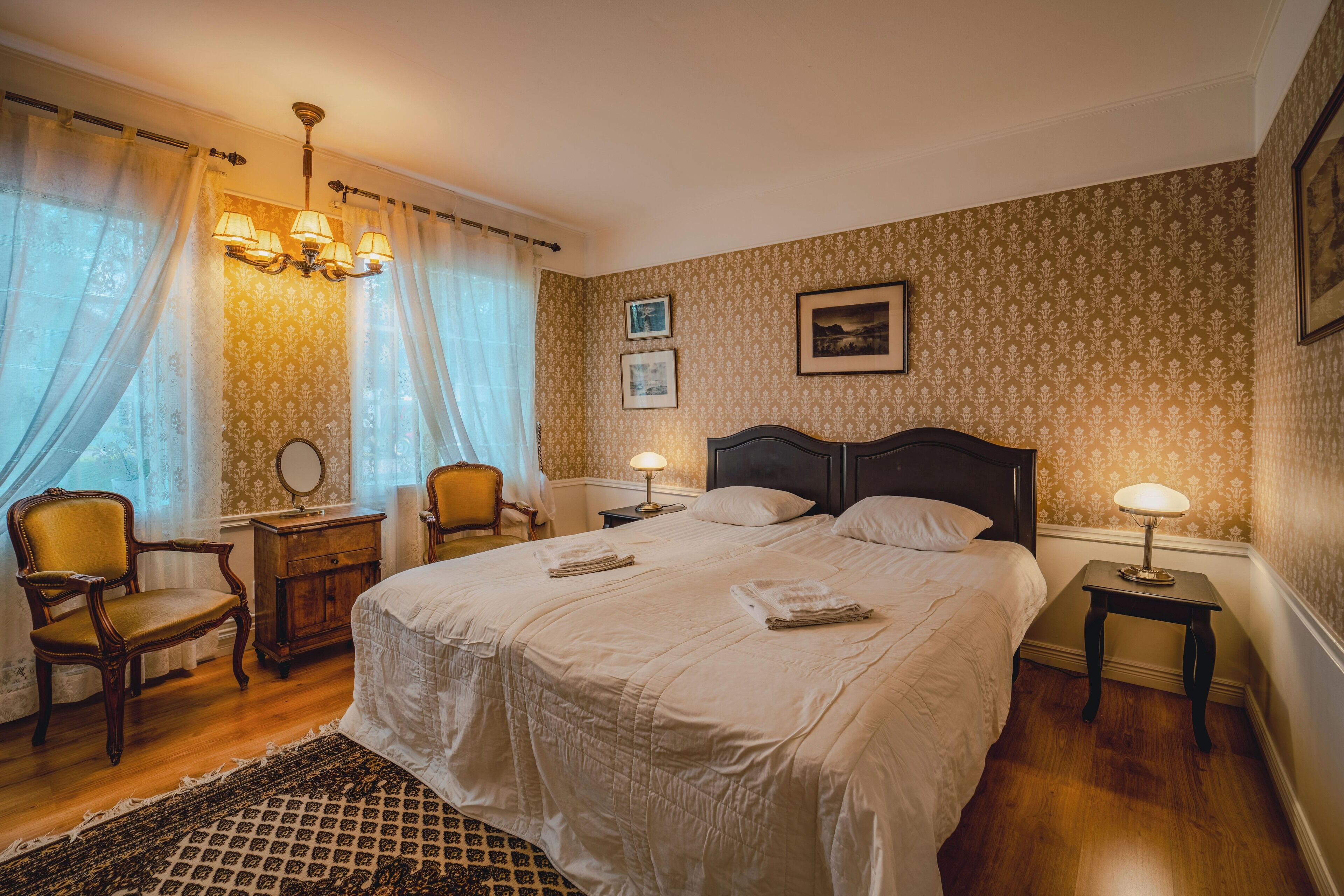 A neatly arranged bedroom with a large bed, two bedside tables with lamps, a chair, and a dresser.
