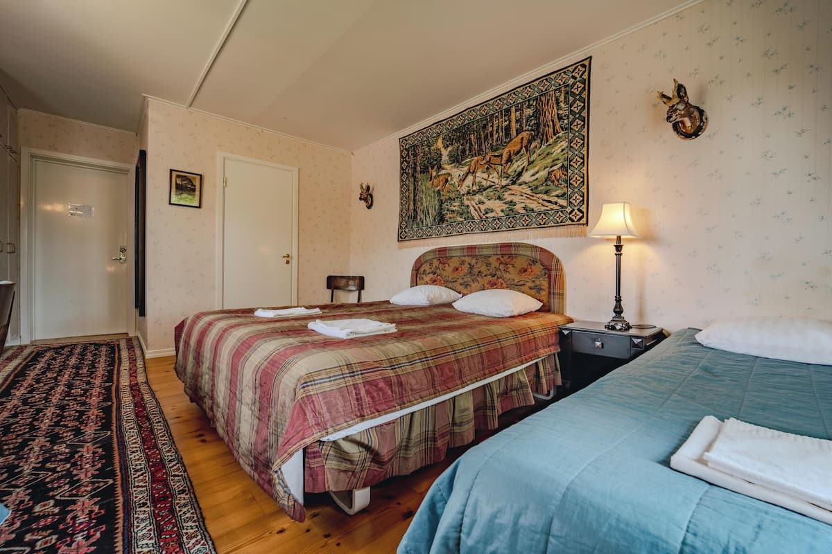 A room with two beds, a patterned rug, a painting, and a lamp.