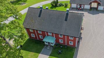An aerial view of a red building with a tiled roof, a covered porch, and a gravel driveway.