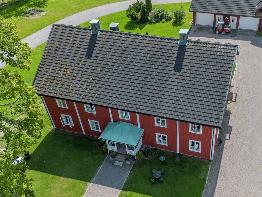 An aerial view of a red building with a tiled roof, a covered porch, and a gravel driveway.