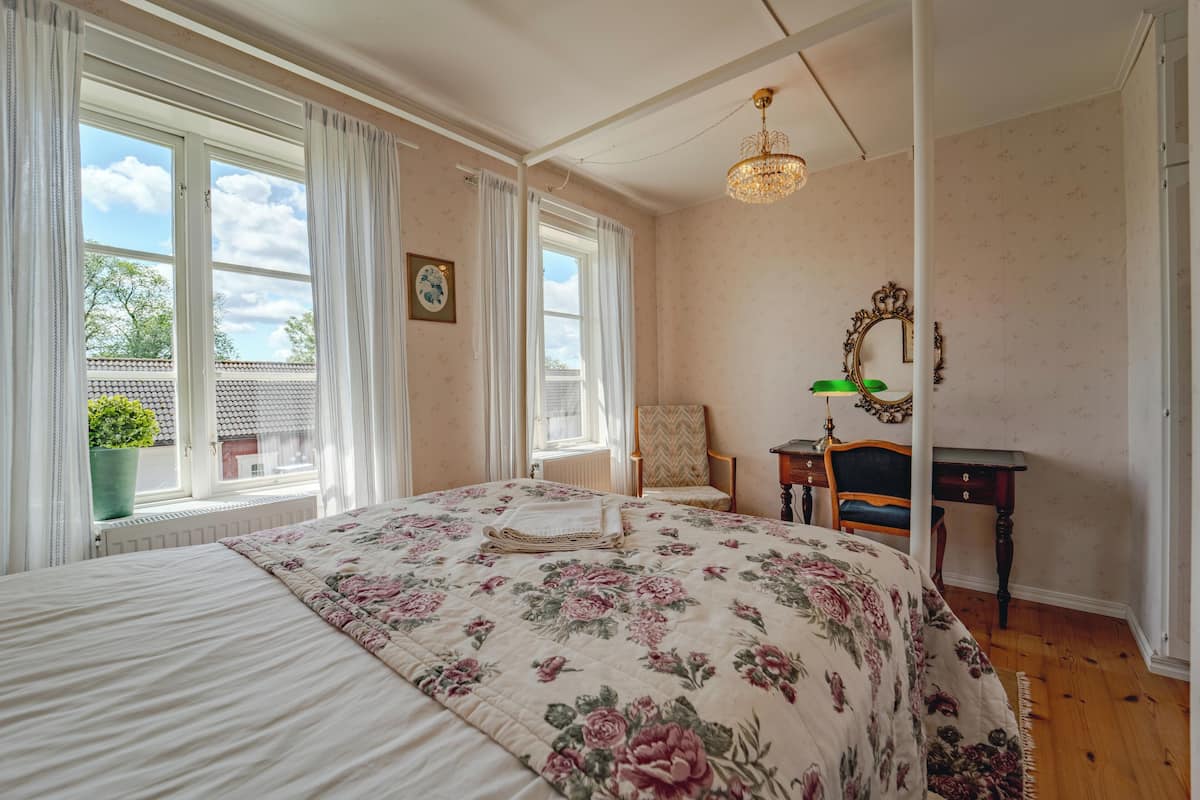 A bedroom with a floral bedspread, a chair, a desk, and a mirror.