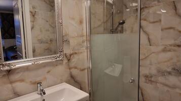 Une salle de bain avec un mur en marbre, une douche en verre, un lavabo blanc et un grand miroir.