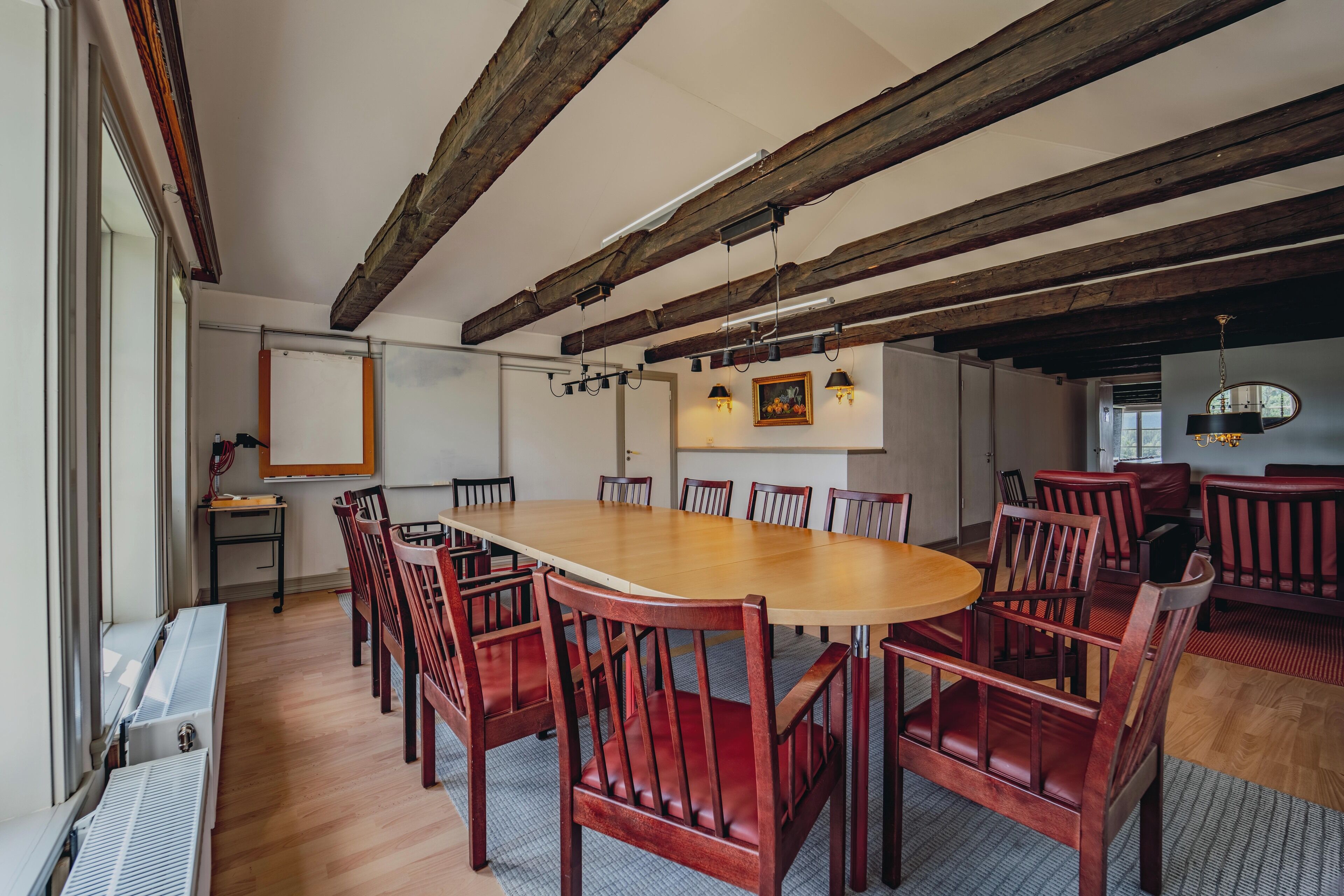 A conference room with a large wooden table and red chairs, wooden beams on the ceiling, and a whiteboard on the wall.