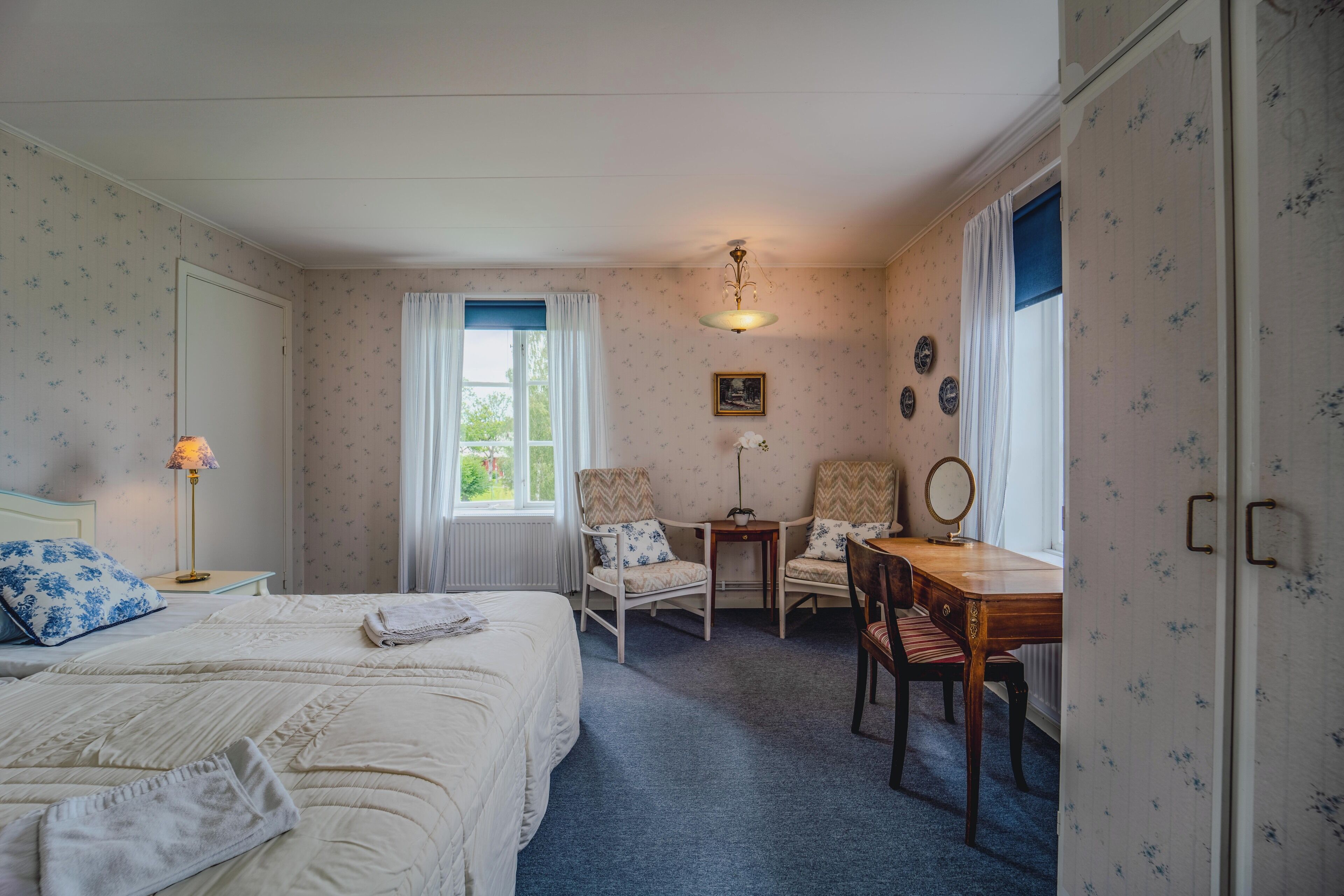 Een slaapkamer met twee bedden, een bureau, stoelen, een spiegel en een raam met gordijnen.