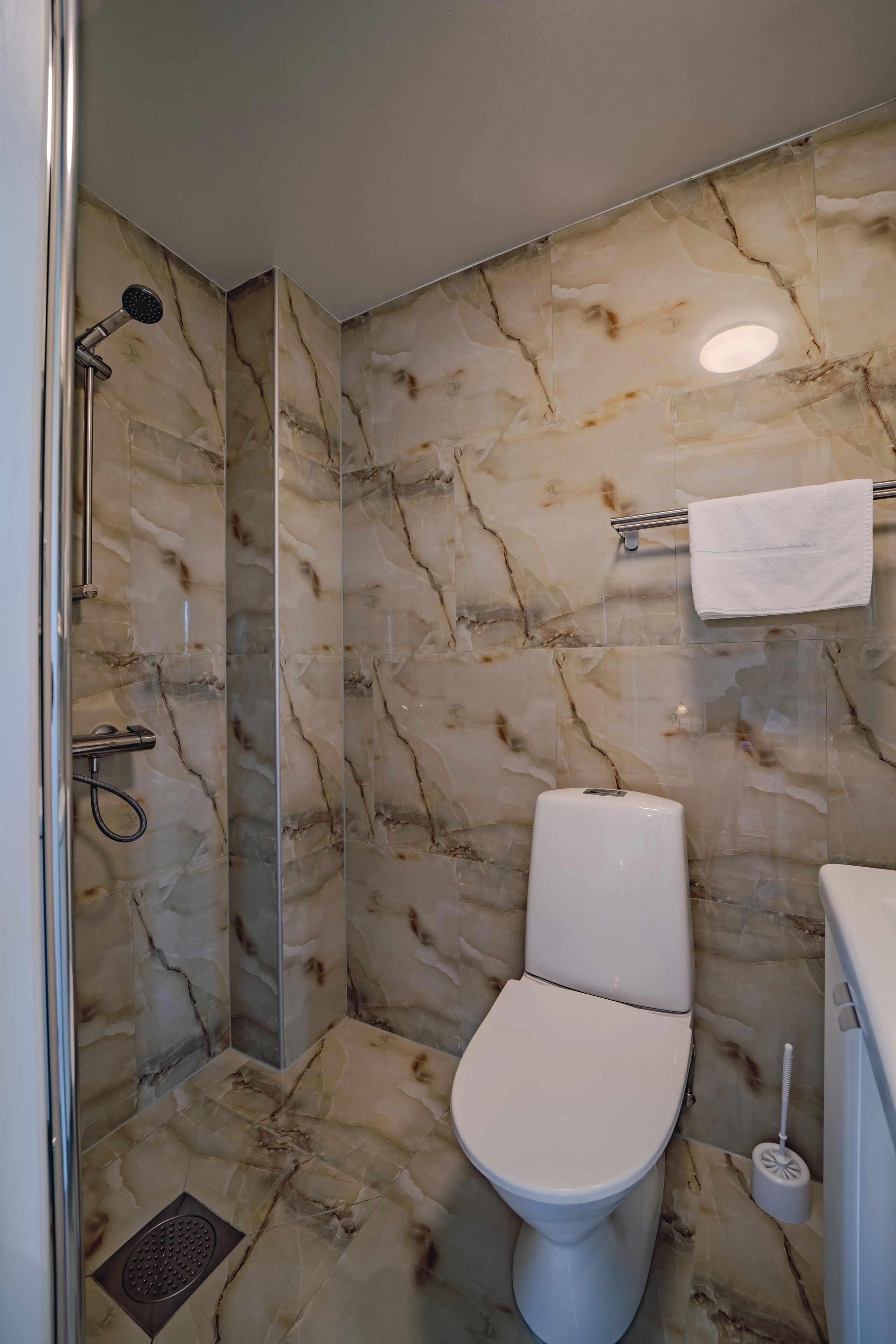 Un baño con ducha, inodoro y paredes de mármol.