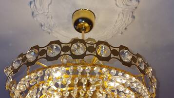 Ein Kronleuchter mit zahlreichen Kristallapplikationen und goldener Rahmen, der an einer kunstvoll gestalteten Decke hängt.