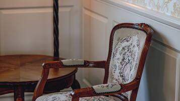 A wooden chair with a floral upholstery, a table, and a lamp with a red shade.