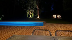 Eine Holzterrasse mit Swimmingpool, einem überdachten Sitzbereich und einem Gebäude mit Kuppeldach.