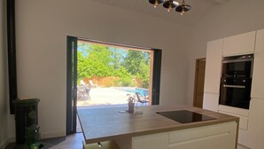 Eine moderne Küche mit einer großen Kochinsel, weißen Schränken und Blick ins Freie.