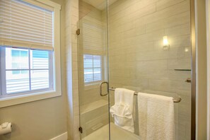 A glass-enclosed shower with a white towel rack, a window with blinds, and a light fixture on the wall. - Aphrodite (Ottawa)