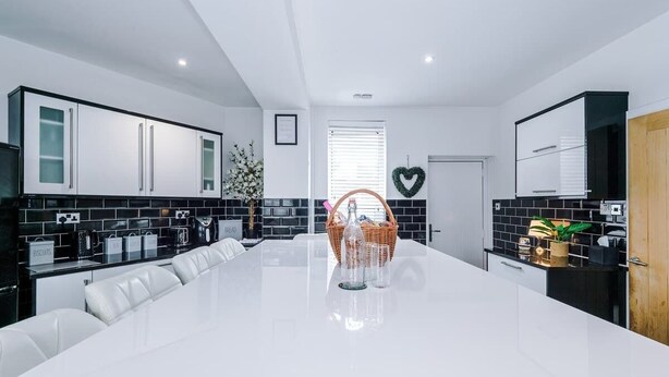 A modern kitchen with a white island, black backsplash, and white cabinetry. - Incredible Home | 3Bedrooms | Driveway | Sleeps 6 (Lancashire)