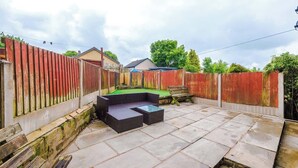 A patio area with a seating arrangement, a stone floor, and a wooden fence. - Incredible Home | 3Bedrooms | Driveway | Sleeps 6 (Lancashire)