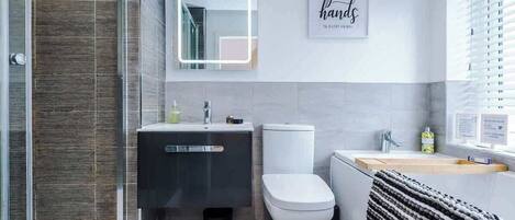Un baño moderno con cabina de ducha de vidrio, inodoro blanco, tocador negro y barra para toallas.