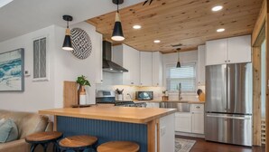 Une cuisine moderne avec un plafond en bois, des armoires blanches, un réfrigérateur en acier inoxydable et un coin bar avec des tabourets.