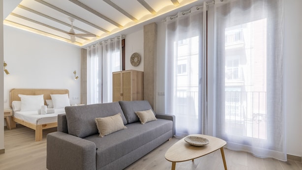 Un salon moderne avec un canapé, une petite table, un lit et de grandes fenêtres ornées de rideaux légers.