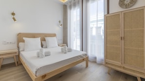 Une chambre à coucher avec un lit en bois, du linge de lit blanc, une table de chevet, une armoire et une fenêtre ornée de rideaux légers.