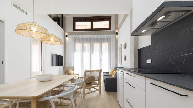 Een moderne keuken met een zwarte marmeren aanrecht, witte kastjes en een eethoek met een houten tafel en rieten stoelen.