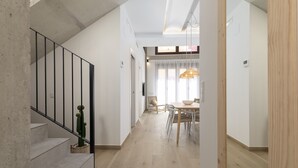 Een trap leidt naar een eethoek met een tafel en stoelen, een hanglamp en een uitzicht op een andere kamer.