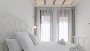 Een wit bed met een metalen hoofdbord, witte kussens en opgerolde handdoeken.