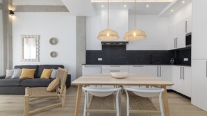 Een moderne keuken met een eetgedeelte, met een lichtkleurige tafel, rieten stoelen en hanglampen.