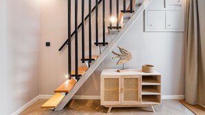 Una escalera moderna con detalles de madera y barandales negros, que conduce a una plataforma con un armario de madera y una escultura decorativa de un pájaro.