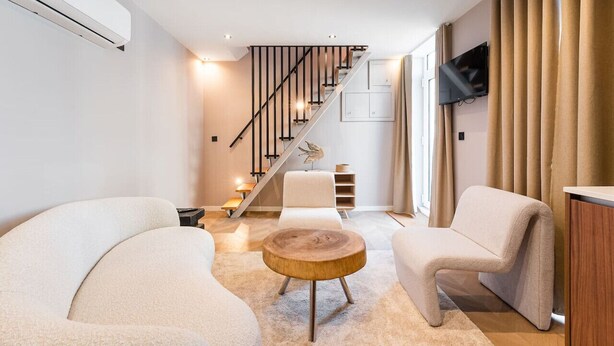 Una sala de estar moderna con una escalera, un televisor de pantalla plana y un ventanal con cortinas.