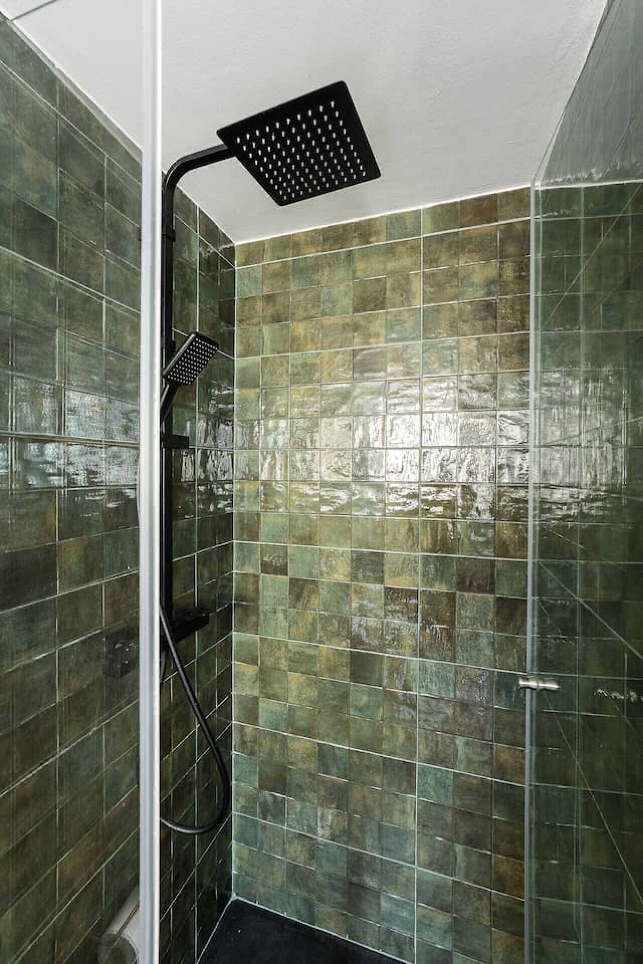 Une douche avec un pommeau de douche noir et une porte en verre.