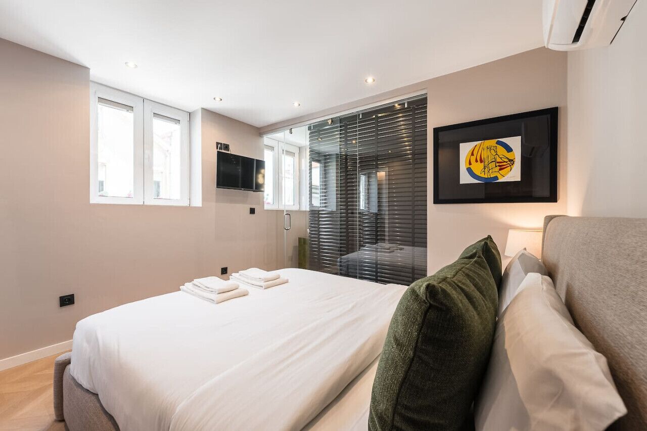 A modern bedroom with a bed, a TV, a framed artwork, and a window.