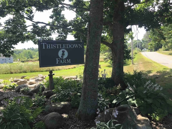 Letrero de Thistledown Farm con un paisaje rural de fondo.