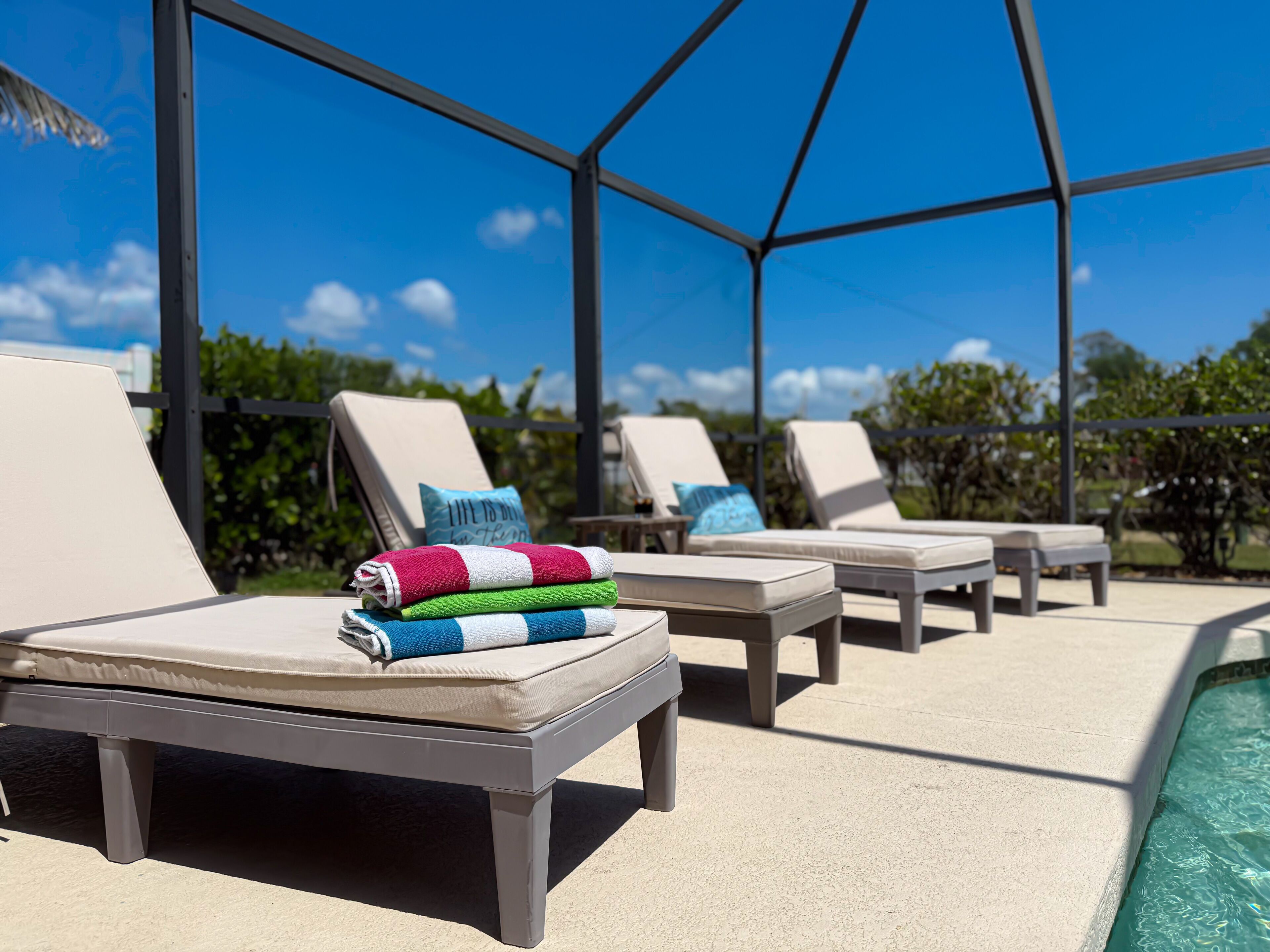 A covered outdoor lounge area with lounge chairs and a pool.