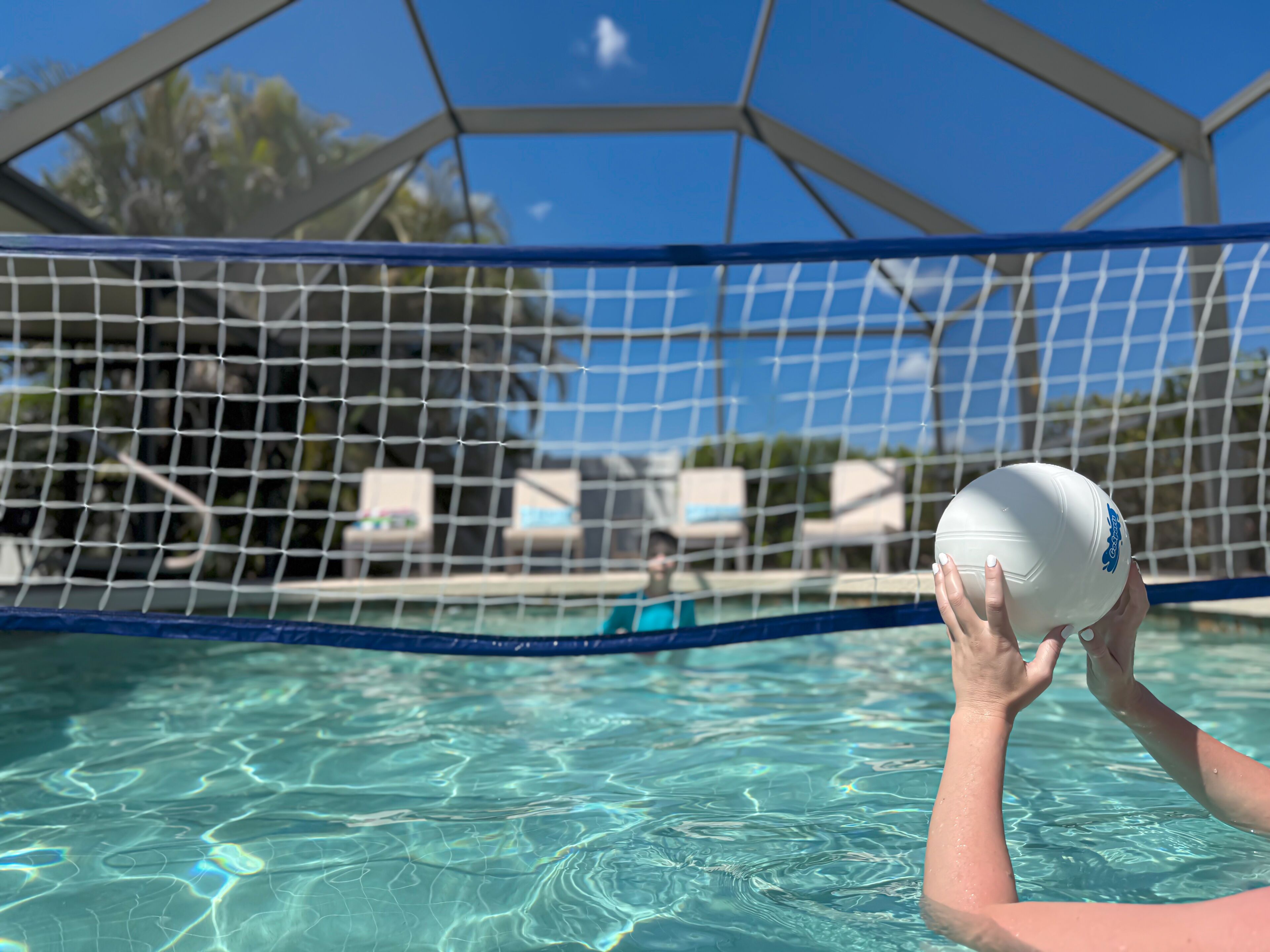 A poolside view with a volleyball net and a person holding a volleyball.