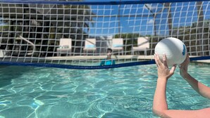 Une vue sur la piscine, avec un filet de volley-ball et une personne tenant un ballon de volley-ball.