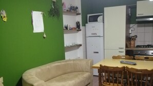 Ein kompakter Wohnraum mit grüner Wand, einem beigen Sofa, einem Esstisch mit Stühlen, einem weißen Kühlschrank und einer Küchenzeile mit Herd.
