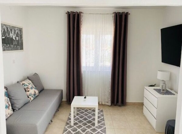 Una habitación pequeña y bien iluminada con un sofá gris, una mesa blanca y un pequeño aparador blanco.