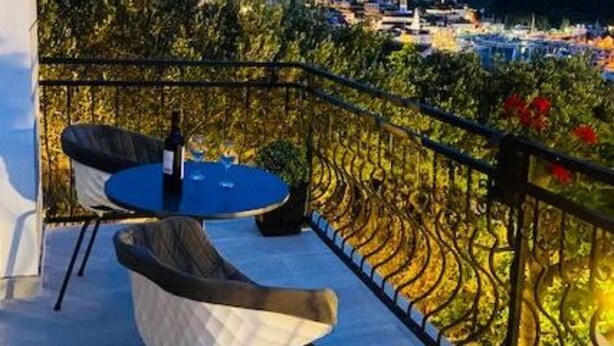 A balcony with two chairs and a table, overlooking a vineyard and a cityscape at dusk. - Villa Brazza - Two Bedroom Apartment 1 (Milna)