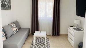 A small, well-lit room with a grey sofa, a white table, and a small white dresser. - Villa Brazza - Two Bedroom Apartment 1 (Milna)