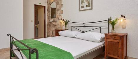 A bedroom with a bed, a nightstand, a wooden cabinet, a stone wall, and a door.
