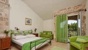 A bedroom with a bed, a green sofa, a wooden nightstand, a green chair, and a stone wall. - Double Bedroom with Balcony (Drvenik Veliki)