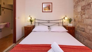 A bedroom with a bed, two bedside tables, a wall-mounted picture, and a stone wall. - Krknjasi - Double Bedroom (Drvenik Veliki)