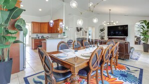 A spacious living room with a large TV, a dining area with a wooden table and chairs, and a kitchen with wooden cabinets. - Port St Lucie Home w/ Above-Ground Pool & Grill (Port St. Lucie)