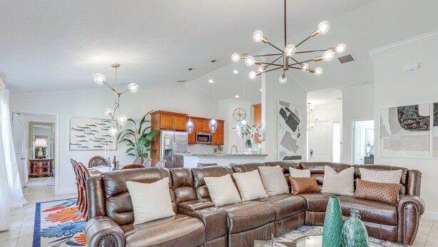 A spacious living room with a leather sectional sofa, a glass coffee table, and a modern chandelier. - Port St Lucie Home w/ Above-Ground Pool & Grill (Port St. Lucie)