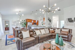 Un salon spacieux avec un canapé d’angle en cuir, une table basse et un lustre moderne.