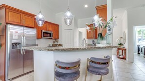 A kitchen with wooden cabinets, stainless steel appliances, a granite countertop, pendant lights, and a central island with bar stools. - Port St Lucie Home w/ Above-Ground Pool & Grill (Port St. Lucie)