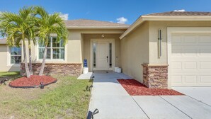 A residential house with a front door, garage, and a landscaped area with palm trees and mulch. - Port St Lucie Home w/ Above-Ground Pool & Grill (Port St. Lucie)