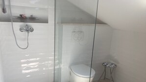A modern bathroom with a glass-enclosed shower, a toilet, and a small stool. - One Bedroom Apartment with Balcony (Sutivan)