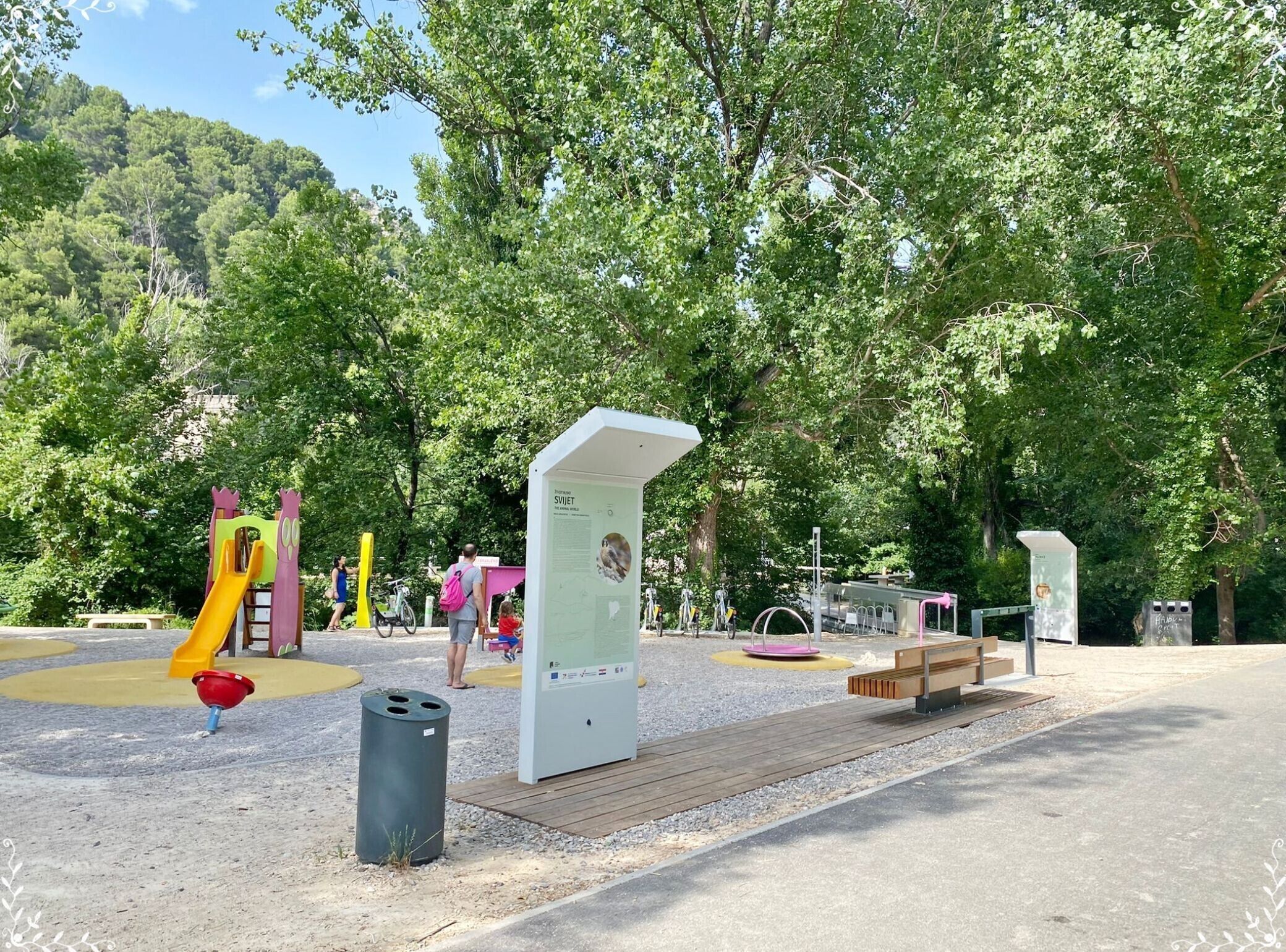 Ein Park mit Spielgeräten, einer Fahrradverleihstation und Informationstafeln.