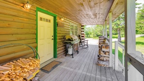 Eine Holzhütte mit Veranda, Grill und Tür mit grünem Rahmen.